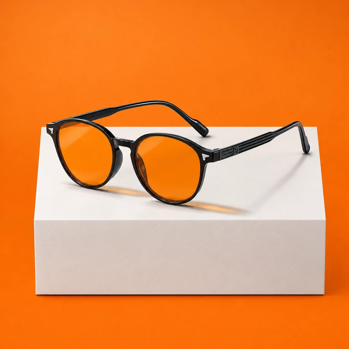 Lunettes du soir moodim, monture ronde noire et verres orange, posées sur un socle blanc