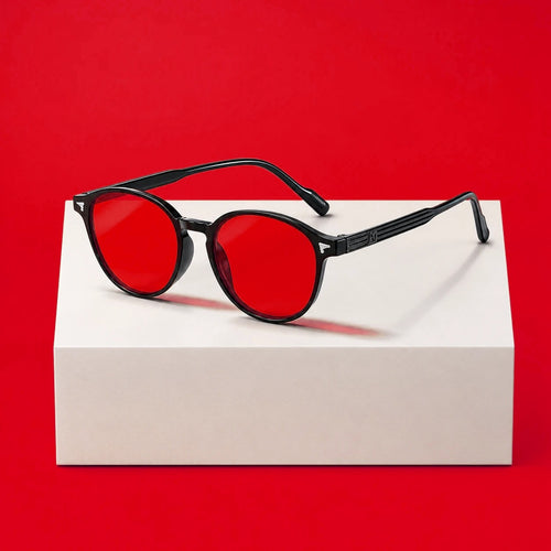Lunettes du soir moodim, monture ronde noire et verres rouges, posées sur un socle blanc